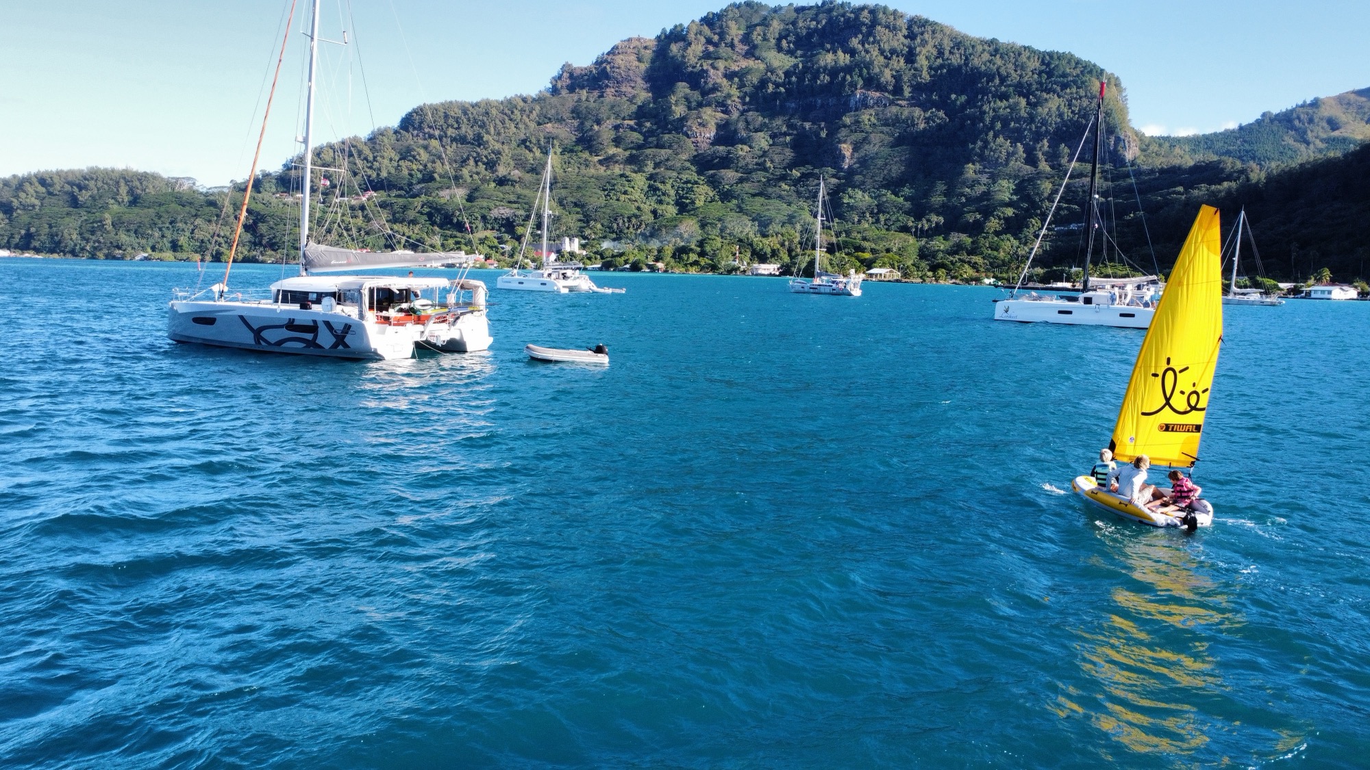 Mouillage devant une île montagneuse de Polynésie française, annexe et petit dériveur à voile jaune